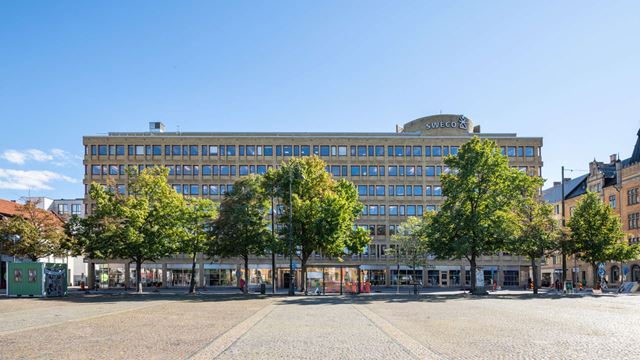 Gul tegelfastighet med Drottningtorget i Malmö i förgrunden.